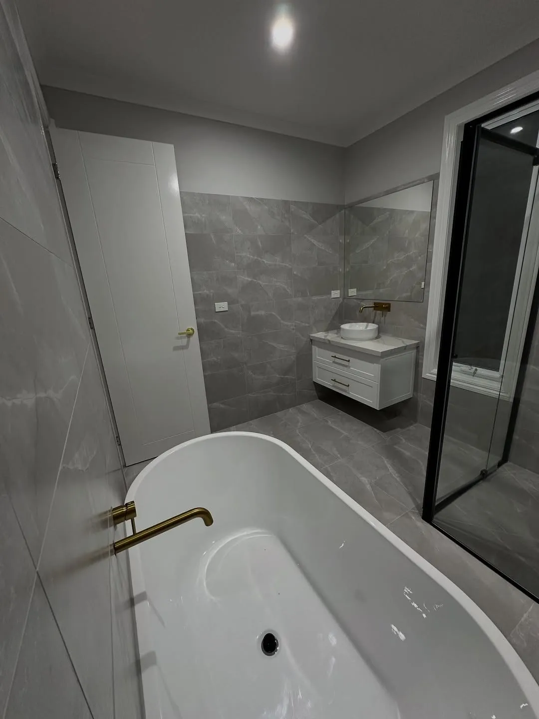 Grey stone bathroom with freestanding bath and gold tapware