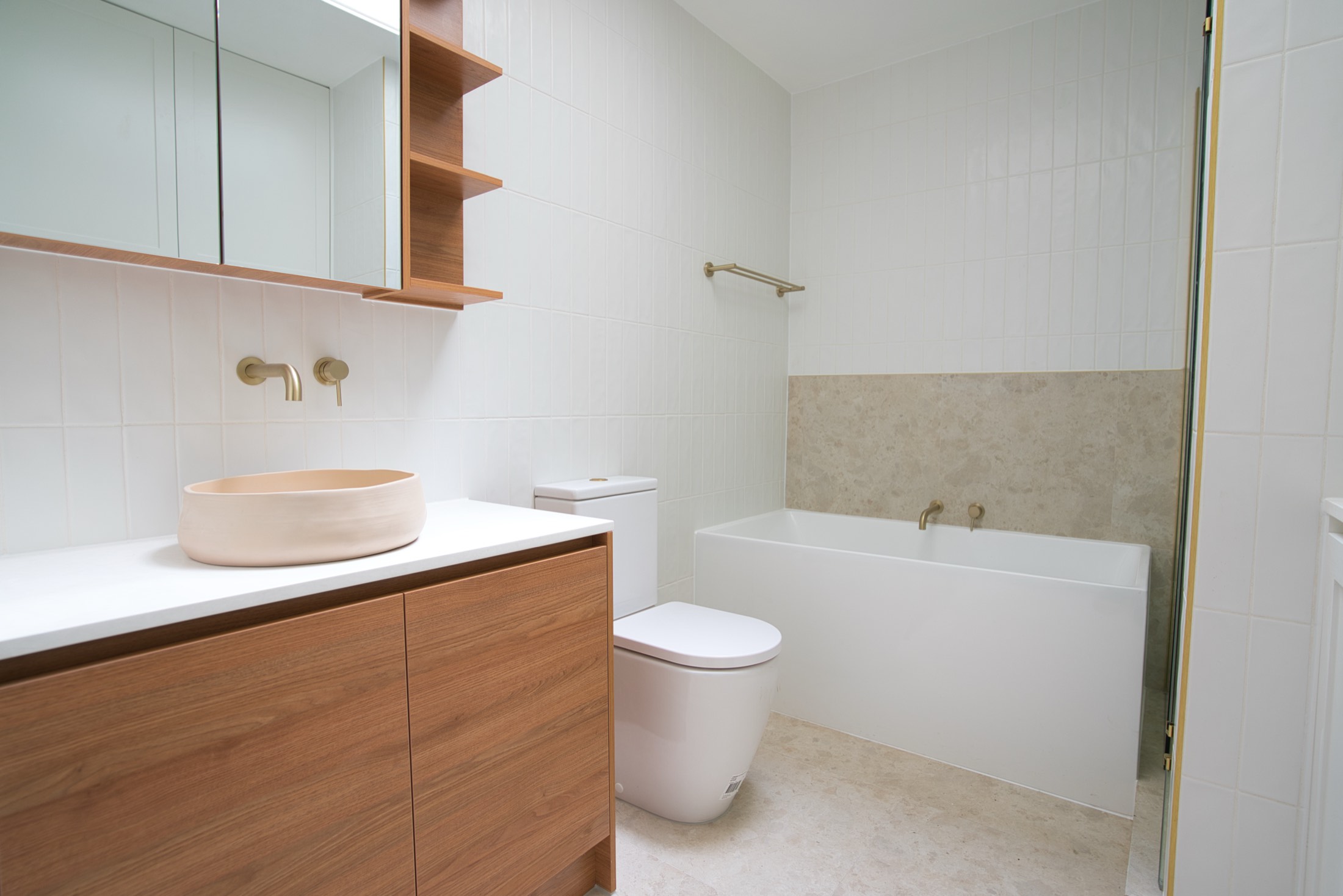 Light-filled bathroom with timber vanity, blush stone basin and brass tapware