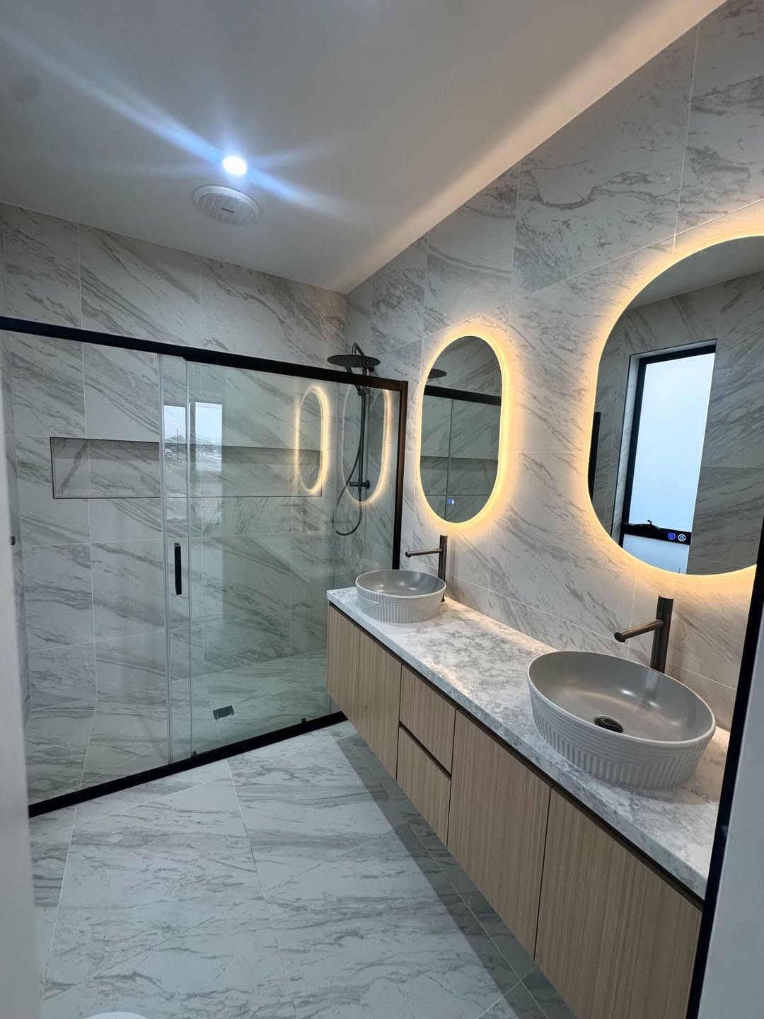 White marble bathroom with double vanity and backlit LED mirrors