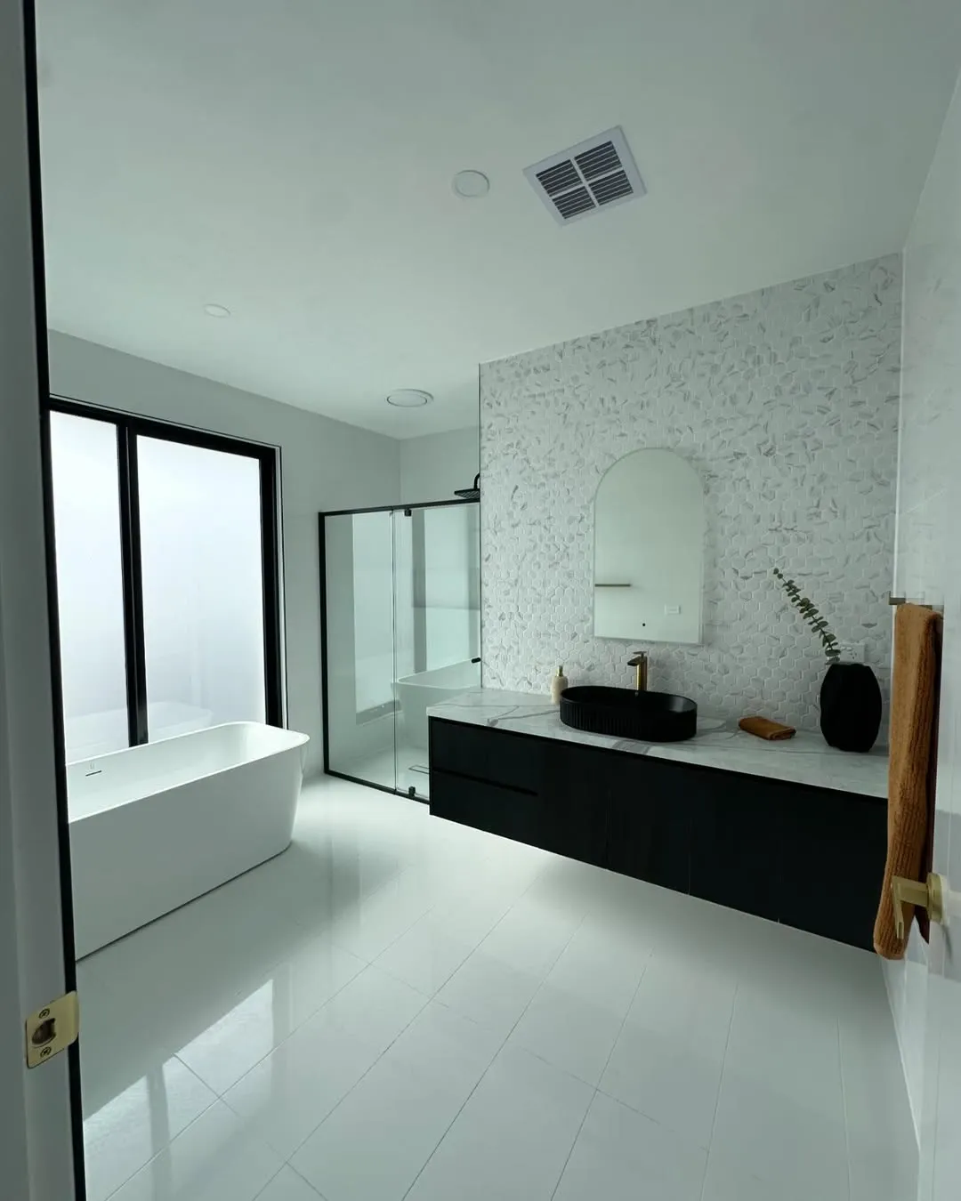 Modern black-and-white bathroom with freestanding bath and hex feature wall